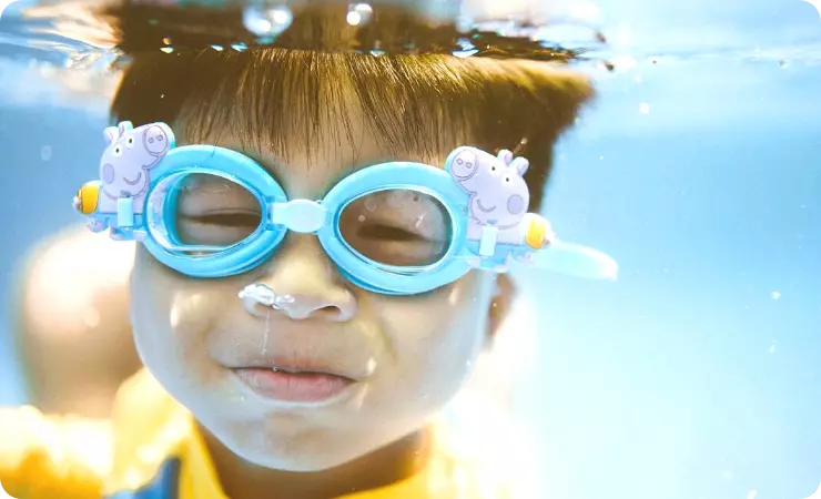 Child wearing the Peppa Pig George blue goggles and submerging his head in the water at the shallow swimming pool for beginners swimming class